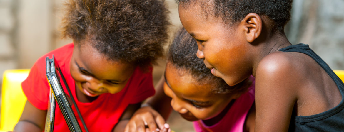 Photo of 3 young children smiling and looking at an iPad.