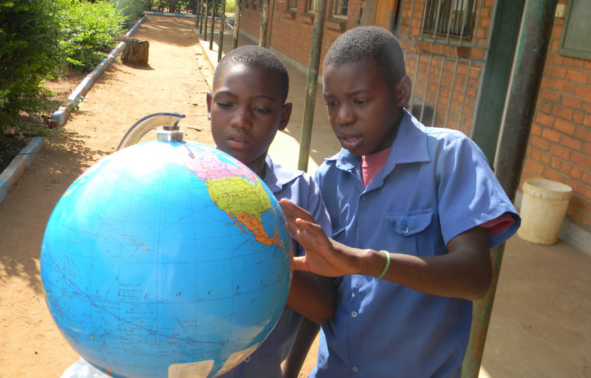 Photo of 2 kids looking at a globe outside.