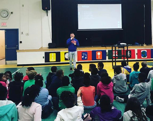 A man gives a talk at a school in DC to a group of students