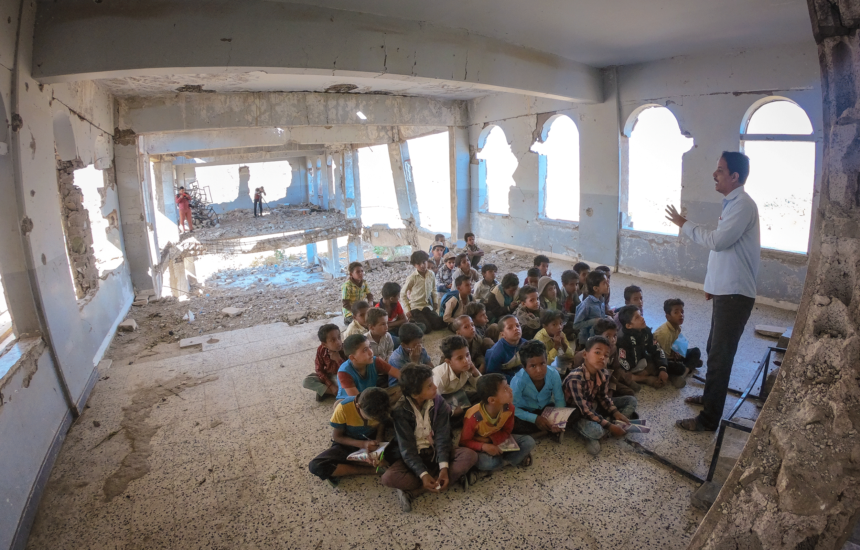 A man teaches a classroom of kids in a rundown building