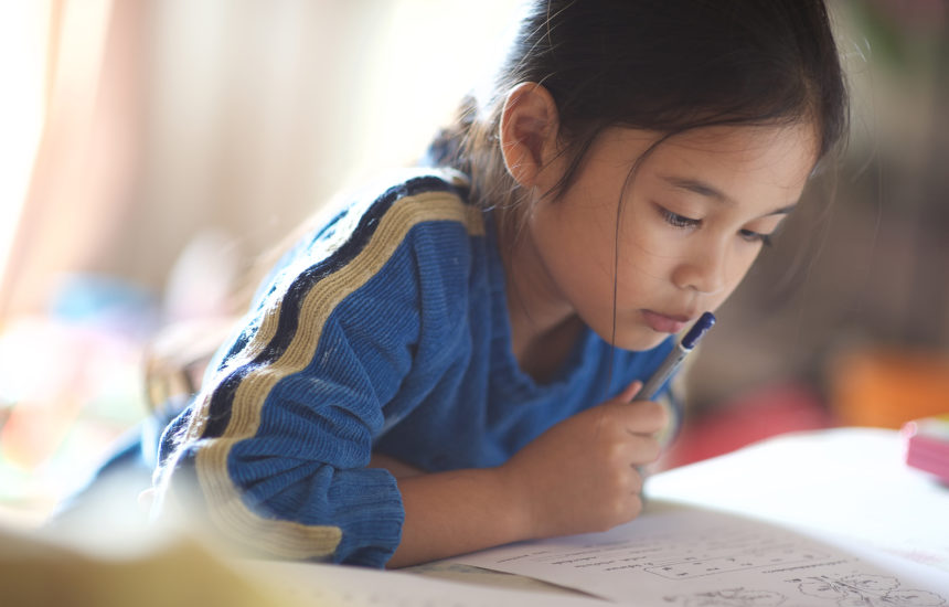 A girl leans over her homework, thinking