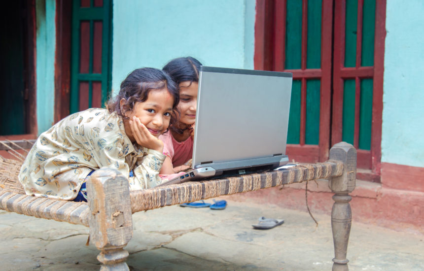 2 girls on a woven bed frame outside working on a laptop