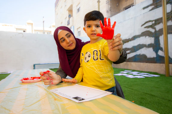 A woman holds up a young boys hand that has red paint on it