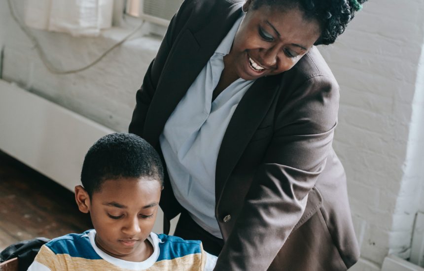 A teacher smiling and pointing to something in a book to show a student