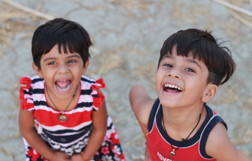 Two young children smiling at the camera. One is wearing a red dress, and the other is wearing a red shirt
