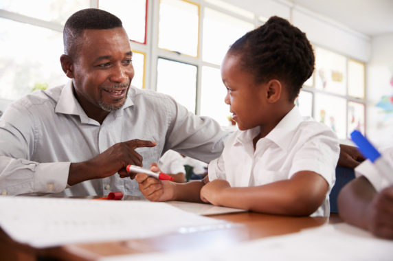 A man helps a child who is writing