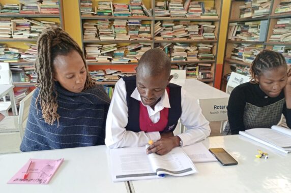 Three people looking at booklets while sitting at a shared desk
