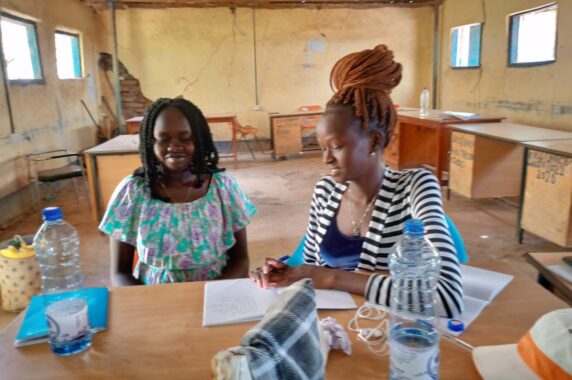 Photo of a teacher with a student, sitting at a table, working together in an empty classroom