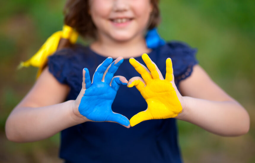 Girl holding her hands to make the shape of a heart. Her hands are painted yellow and blue for Ukraine.
