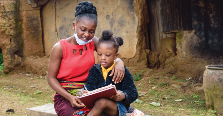 A teacher reading with a young student outside of a school in Africa