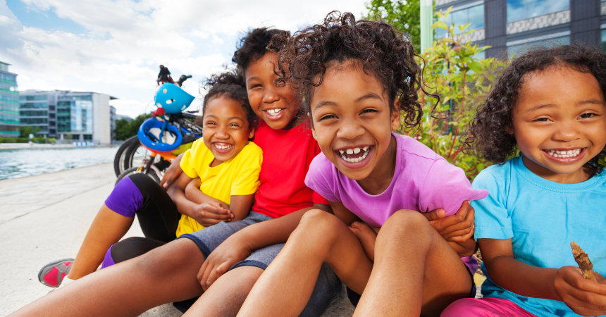 Four smiling young children with toys outdoors near buildings