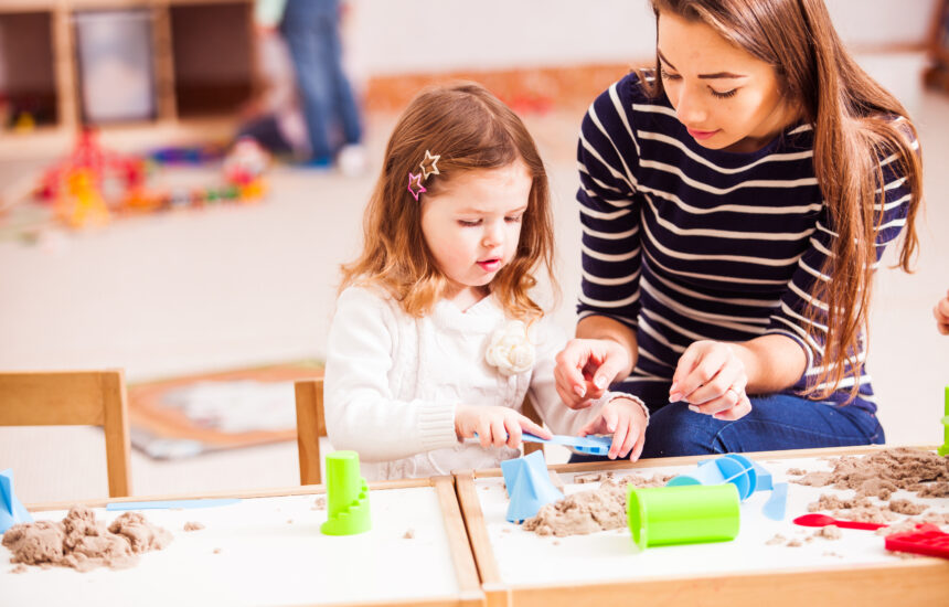 A teacher helps a young girl create things using sand
