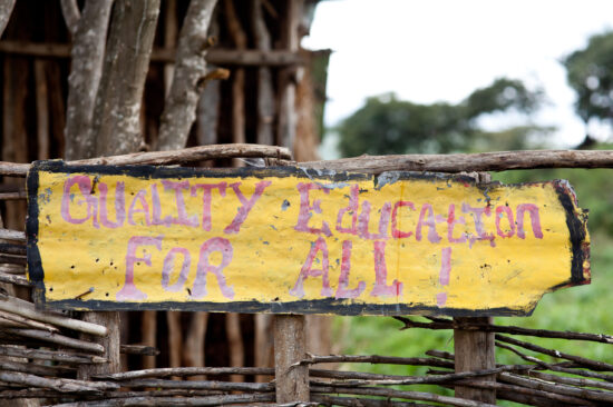 A homemade yellow banner strung on a tree outdoors with painted words that say, "Quality education for all."