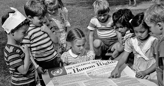A black-and-white historical photo of children standing around the Declaration of Human Rights.