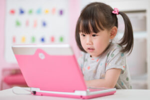 A young girl with dark hair and light skin happily looking at a print laptop.