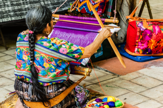 A woman in Guatemala sitting on the ground, weaving a colorful tapestry