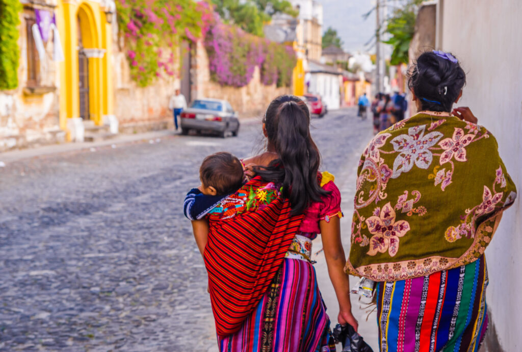 2 women walk outside while carrying a child.