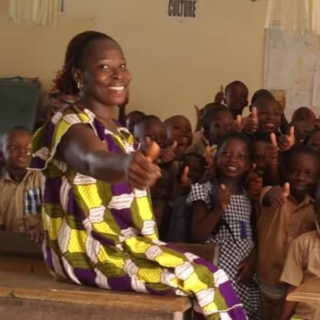 A woman smiles and gives a thumbs up with a group of students in a classroom