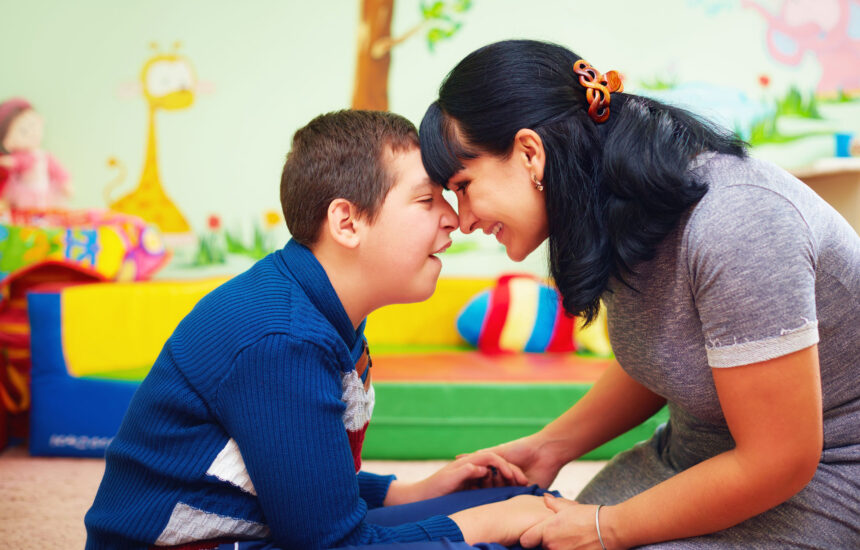 A woman puts her head against a young boy's head, smiling