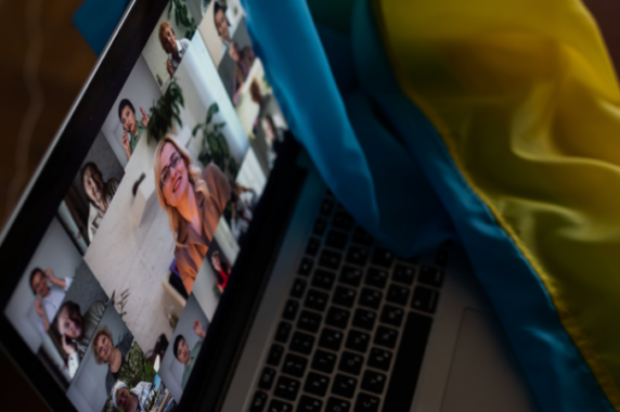 A laptop with video squares of multiple people at an online training. Next to the laptop is the Ukrainian flag.