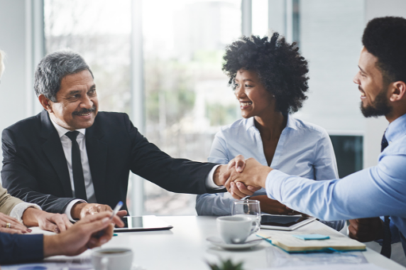 Three people happily shaking hands around a table.