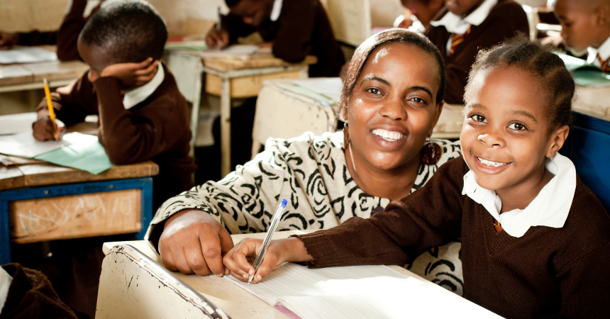 A happy, smiling teacher next to a happy student in the classroom.