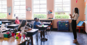 A teacher in front of a classroom, happily teaching students.