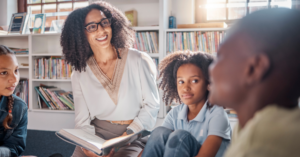 A happy teacher reading to students in a classroom.