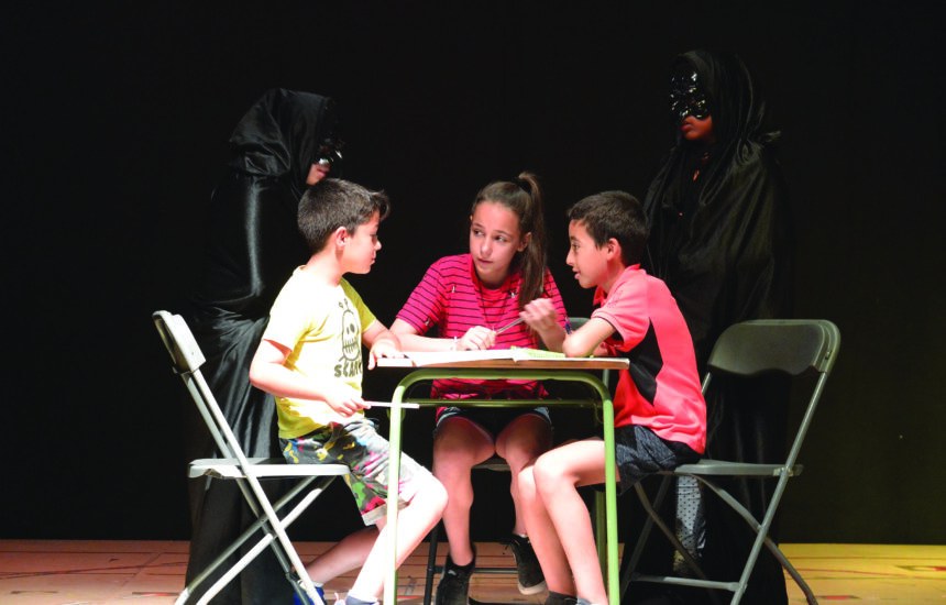 Three children sitting at a table as part of a theater.