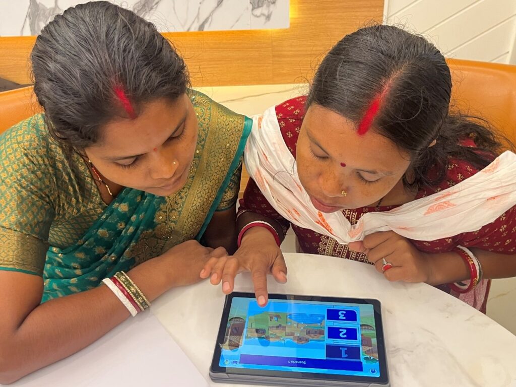 Two women sit at a table, using the Coach Up app on a tablet.
