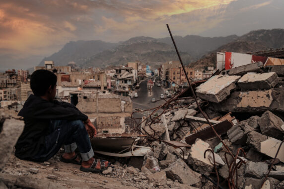 A child sits in the ruins of a destroyed city.